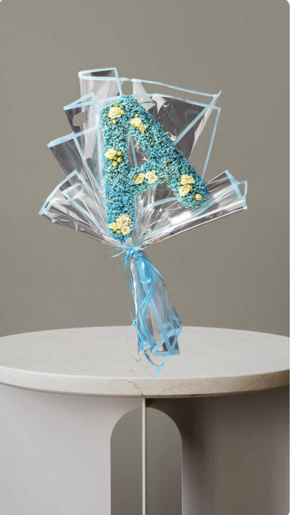 دسته گل با طراحی حرف a ساخته شده از گلهای آبی و کرم با کاغذپیچی شفاف و روبان آبی مناسب هدیه تولد و سورپرایز