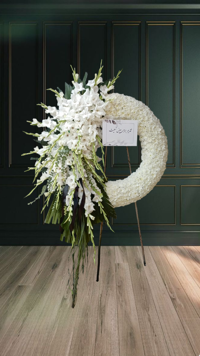 تاج گل تسلیت سفید با طراحی نیم‌دایره‌ای از گل‌های گلایل و داوودی سفید مناسب مراسم ترحیم